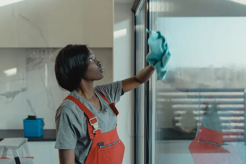 A woman wipes a window pane with a cloth.